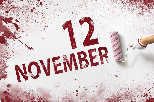 12 ноября. День 12 месяца, дата календаря. Рука держит ролик с красной краской и пишет дату календаря на белом фоне. Осенний месяц, день года - Фото, изображение