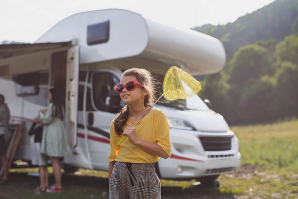 Happy small girl with sunglasses standing outdoors by caravan car, family holiday trip. - Foto, afbeelding