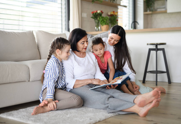 Happy small girls with mother and grandmother indoors at home, reading story book. - Photo, Image