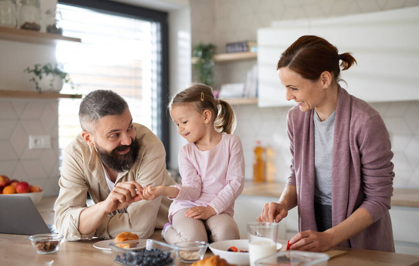 Οικογένεια με μικρή κόρη σε εσωτερικούς χώρους στην κουζίνα στο σπίτι, καθημερινή ζωή και γραφείο στο σπίτι με την έννοια του παιδιού. - Φωτογραφία, εικόνα