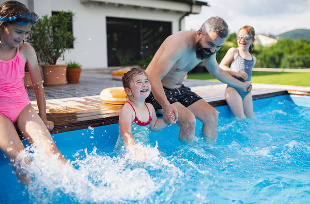 Father with three daughters outdoors in the backyard, playing in wimming pool. - Foto, imagen
