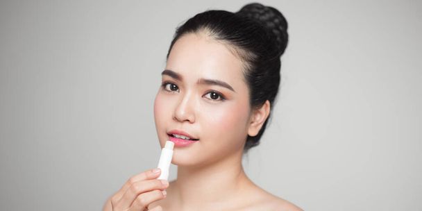 Asian woman applying hygienic lip balm over grey background - Фото, зображення