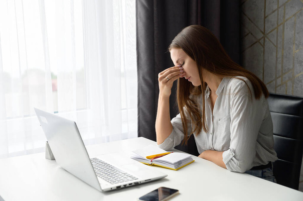 Upset stressed worried woman sitting in front of laptop, holding bridge of the nose - Foto, Imagen