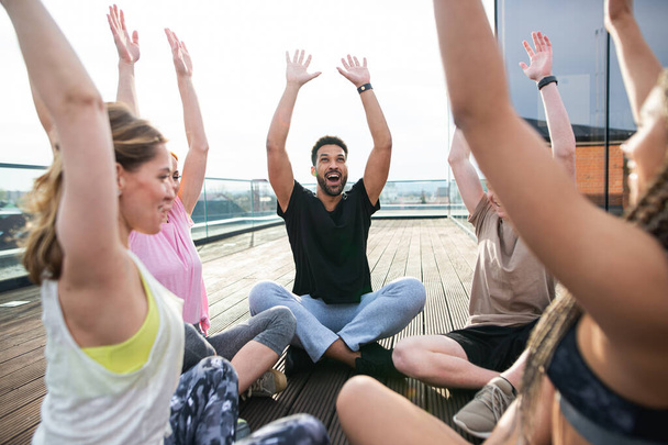 Grupo de jóvenes haciendo ejercicio al aire libre en terraza, deporte y estilo de vida saludable. - Foto, Imagen