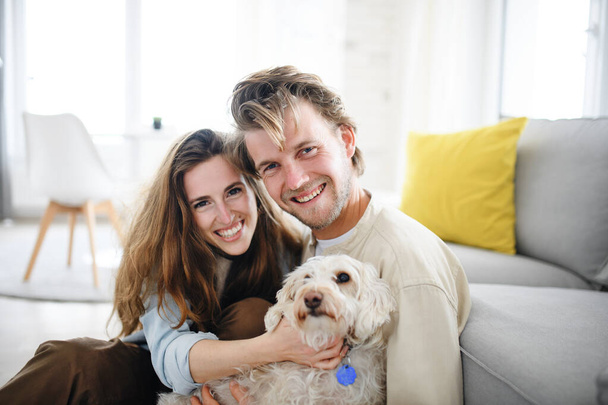 幸せな若いカップルで愛犬と屋内で自宅で、カメラを見て. - 写真・画像