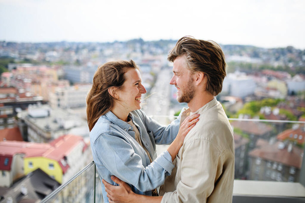 Happy young couple in love standing outdoors on balcony at home, looking at each other. - Fotografie, Obrázek