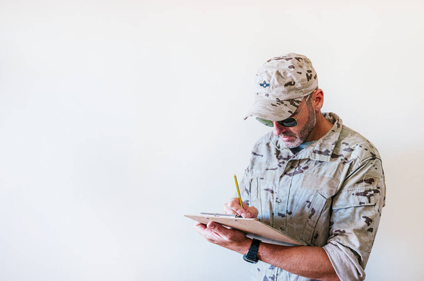 Uomo caucasico in uniforme militare camuffata che scrive nel taccuino. - Foto, immagini