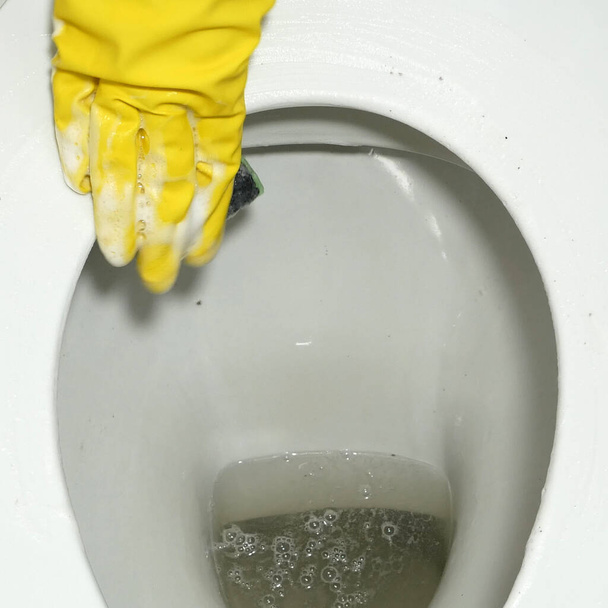 Hände in gelben Gummihandschuhen reinigen die Toilette. Toilette mit Toilettenbürste reinigen Nahaufnahme - Foto, Bild