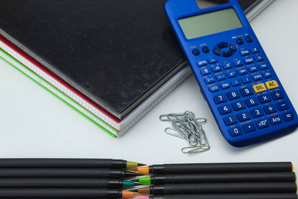 groupe d'outils scolaires avec cahiers, marqueurs, stylos, clips et calculatrice prêts pour la rentrée scolaire sur fond blanc - Photo, image