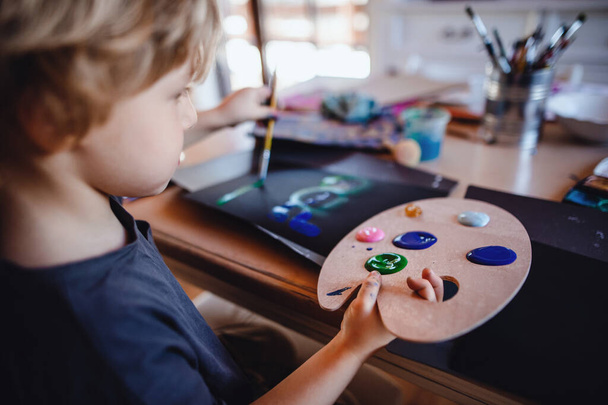 Concentrated small boy painting pictures indoors at home, leisure time. - Photo, Image