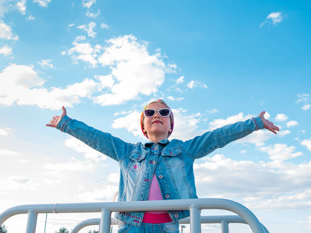 Pieni vaalea tyttö, jolla on kohotetut kädet sininen pilvinen taivas tausta. Onnellinen lapsi lentelee ilmassa. Elämäntapa matkustaa oikeita ihmisiä ulkona. Perhe kävely hauskaa loma Vapaus onnea käsite - Valokuva, kuva