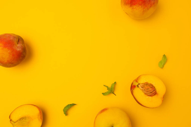 Спелые персики с мятными листьями изолированы на желтом фоне с копировальным пространством для текста. Вид сверху. Плоский узор. Состав продуктов - Фото, изображение