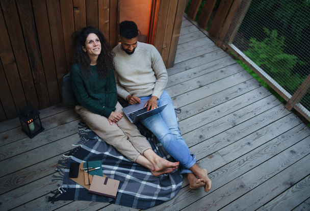 Draufsicht auf glückliches Paar mit Laptop, das im Freien in einem Baumhaus ruht, Wochenendausflug und entferntes Bürokonzept. - Foto, Bild