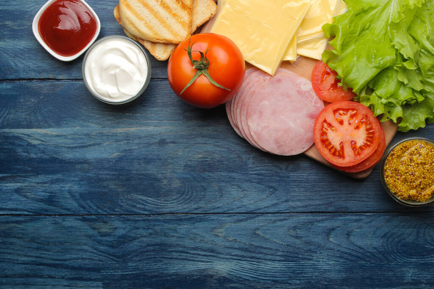 Σάντουιτς. Συστατικά για την παρασκευή σάντουιτς ζαμπόν, τυρί, ντομάτα σε μπλε φόντο - Φωτογραφία, εικόνα