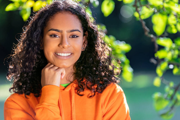 Outdoor portrait of beautiful happy mixed race African American girl teenager female young woman thinking and smiling with perfect teeth with a natural green leaves background - Valokuva, kuva