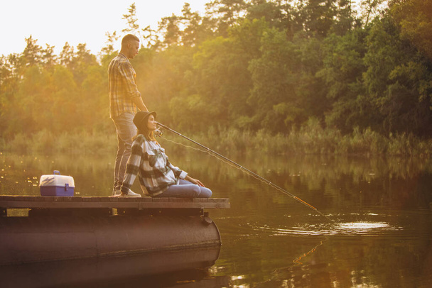 Genç bir çift sıcak yaz gününde gün batımında iskelede balık tutuyor. - Fotoğraf, Görsel
