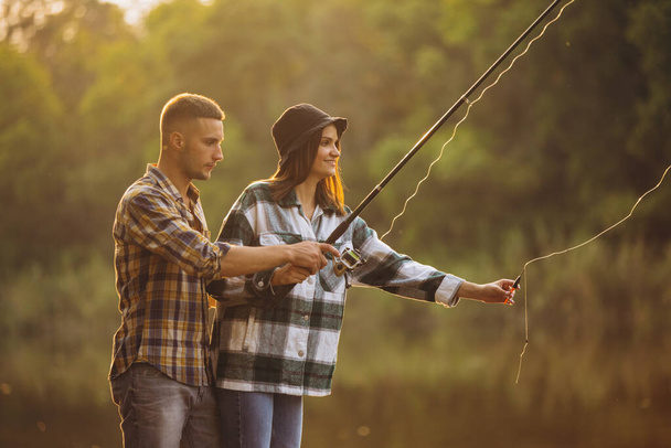 Portrait of young couple fishing on warm summer day in countryside at sunset - 写真・画像