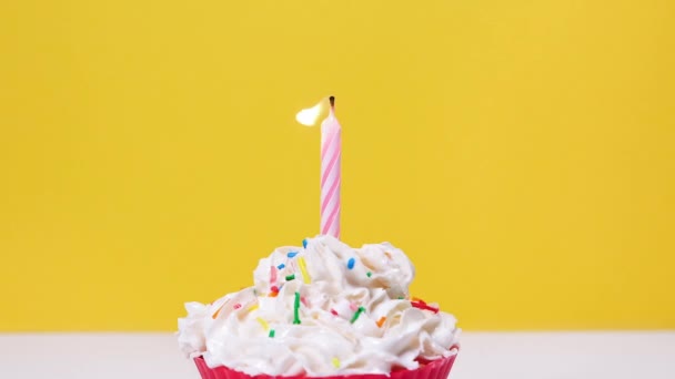 ホイップクリームと黄色の背景に隔離された1つの燃焼ケーキキャンドルでおいしいカップケーキのビューを閉じます。ケーキのろうそくを１本消しなさい。フルHDスローモーション幸せな誕生日や記念日ビデオ - 映像、動画