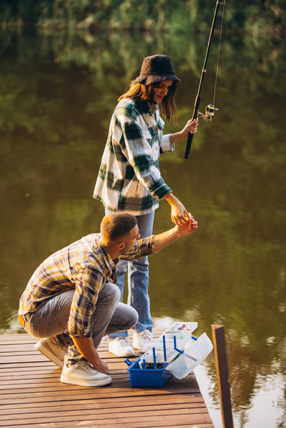 Vertical portrait of young couple fishing on warm summer day in countryside at sunset - Photo, Image