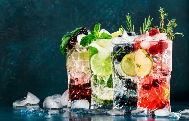 Cocktails drinks. Classic alcoholic long drink or mocktail highballs with berries, lime, herbs and ice on blue background - Photo, image