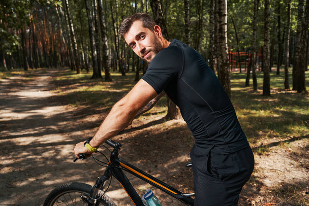 Smiling handsome male riding bike in nature - Valokuva, kuva