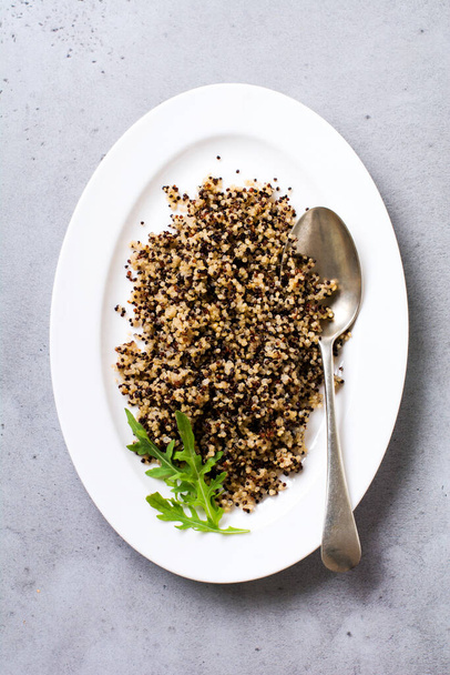Cooked white, red and black quinoa in white plate on grey rustic background, top view, place for text recipes or menu. Vegan Superfood, healthy eating and nutrition or diet concept. - Foto, Bild