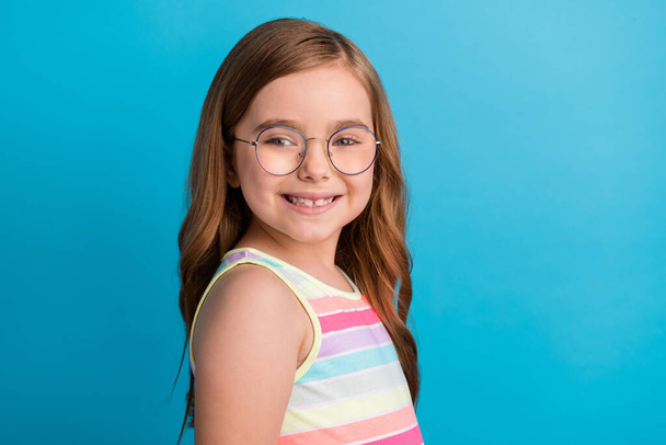 Photo of cute lovely little girl toothy beaming smile wear specs striped dress isolated blue color background - Foto, afbeelding