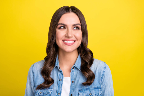 Photo of charming dreamy young lady wear jeans shirt smiling looking empty space isolated yellow color background - Photo, Image