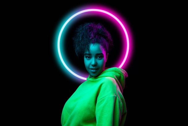 Portrait of african happy smiling girl in neon light on dark studio background with neoned blue circle. Concept of youth, music, disco, ad, sales - Foto, Bild
