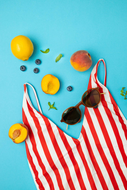 Gafas de sol femeninas, bañador y frutas sobre un fondo azul brillante. Asiento plano, vista superior. Viajes verano concepto - Foto, Imagen