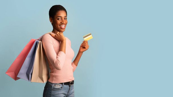 Cashback Concept. Jonge zwarte vrouw met een creditcard en lichte boodschappentassen - Foto, afbeelding