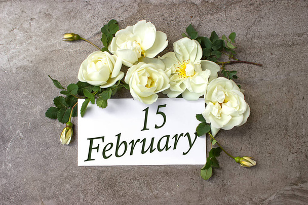 Le 15 février. Jour 15 du mois, date du calendrier. Roses blanches bordent sur fond gris pastel avec la date du calendrier. Mois d'hiver, concept de jour de l'année - Photo, image