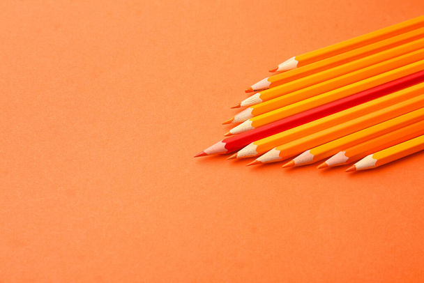 Punainen lyijykynä oranssien joukossa väritaustalla. Ainutlaatuisuuden käsite - Valokuva, kuva
