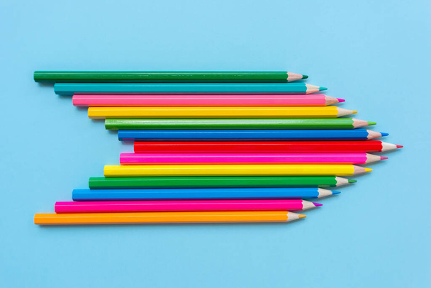Цветные карандаши сложены в форме стрелки, указывающей направление на голубом фоне. Концепция разнообразия, связи и движения в одном направлении. - Фото, изображение
