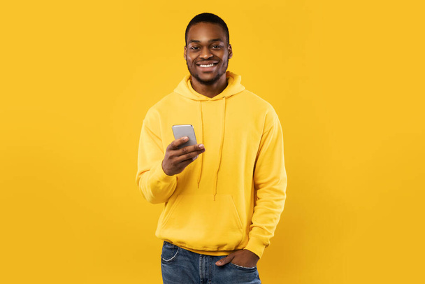 Glücklicher schwarzer Millennial-Mann mit Handy über gelbem Hintergrund - Foto, Bild