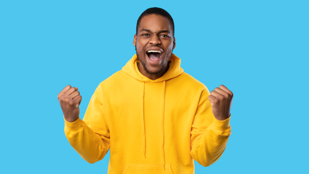Emotionele Afro-Amerikaanse man schudden vuisten schreeuwen over blauwe achtergrond - Foto, afbeelding