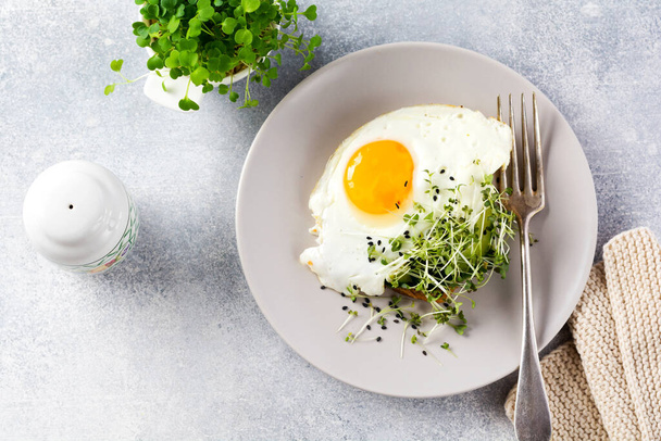 Fried eggs with arugula microgreen in gray ceramic plate on gray concrete old background. Traditional English breakfast. Top view - Foto, imagen