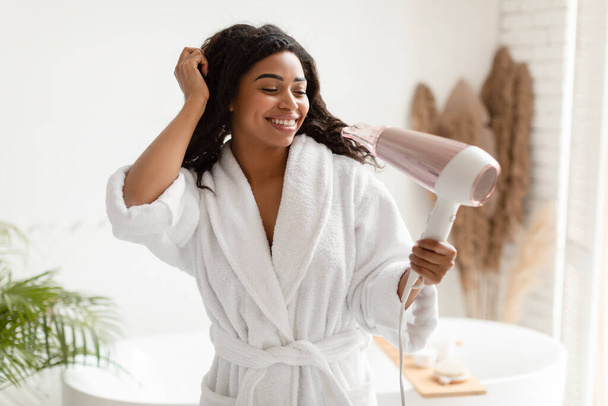 Joyeuse femme noire utilisant sèche-cheveux séchage cheveux humides dans la salle de bain - Photo, image