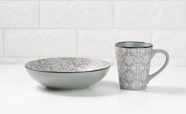 порожня сіра керамічна супова тарілка та порожня чашка на білому столі, посуд
 - Фото, зображення