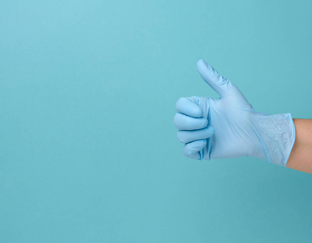 hand in a blue latex medical disposable glove shows the gesture like on a blue background, approval and consent - Photo, Image