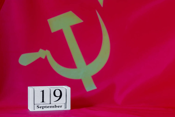 Der 19. September auf einem hölzernen Kalender vor dem Hintergrund der Flagge der Kommunistischen Partei. - Foto, Bild