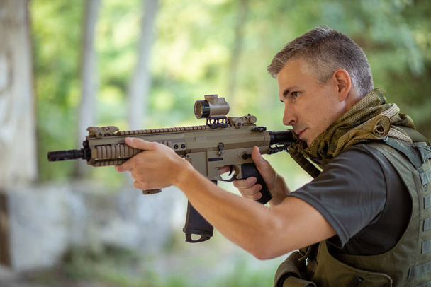 Un uomo con un fucile d'assalto airsoft in uniforme militare nella foresta - Foto, immagini