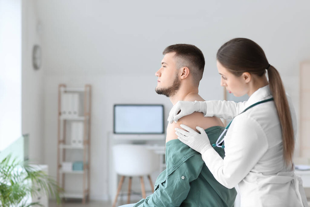 Medico applicando intonaco sulla spalla del giovane in clinica - Foto, immagini