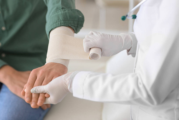 Medico che applica benda sul braccio del giovane in clinica, primo piano - Foto, immagini