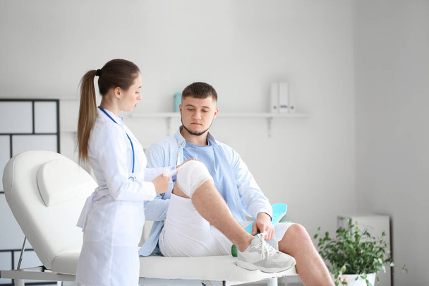Doctor applying bandage onto knee of young man in clinic - Φωτογραφία, εικόνα