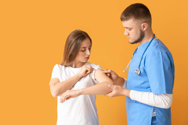 Doctor applying plaster onto arm of young woman on color background - Фото, зображення