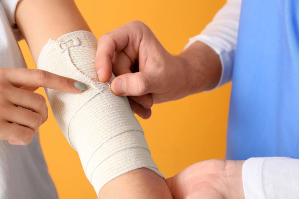 Médecin appliquant bandage sur le bras de la jeune femme sur fond de couleur - Photo, image