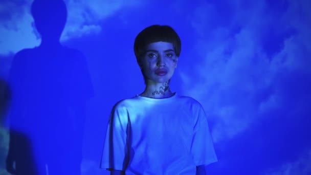 Young tattooed model on blue background with clouds  - Кадры, видео