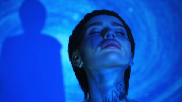 Modelo tatuado con ojos cerrados sobre fondo azul abstracto  - Metraje, vídeo