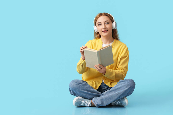Mature woman with headphones reading book on color background - Fotó, kép